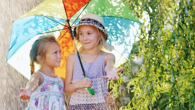 Two girls 4 and 6 years of hiding under colorful umbrellas. Warm summer rain, the children are happy