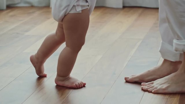 Side view of barefoot legs of baby in diaper walking towards his mother moving backwards