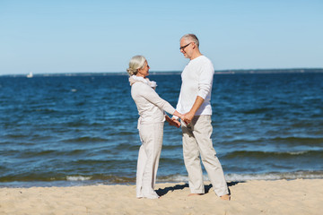 happy senior couple holding hands on summer beach