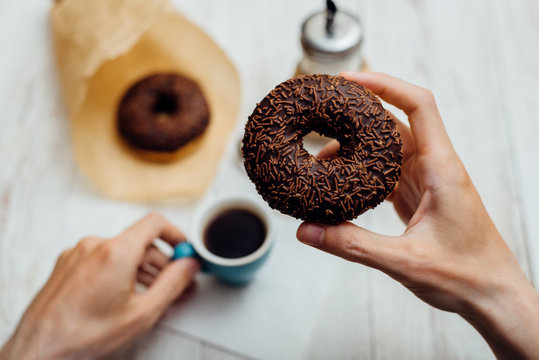 Man hands eating chocolate donut with coffee on wooden table