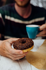Man hands eating chocolate donut with coffee on wooden table