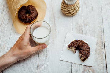 Man hands eating chocolate donut with coffee on wooden table