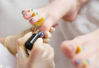 Pedicurist applying nail polish, close up photo