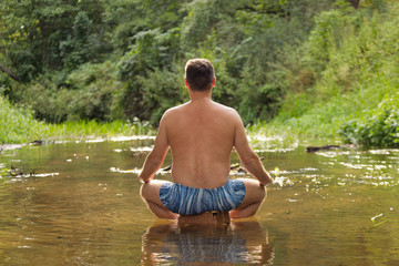 a man meditating in the middle of the water forest river