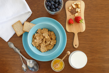 breakfast of cereal, fruit, cookies in a blue plate on a brown wooden table. view from above. a table for breakfast.