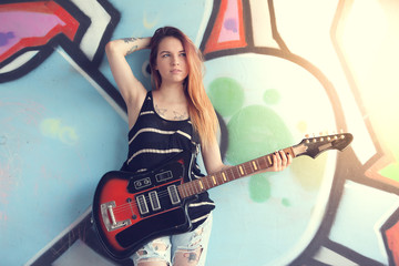 Girl with electric guitar near graffiti wall.