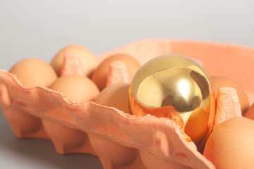 Cardboard egg box with golden and chicken eggs on gray backgroun