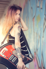 Obraz premium Girl with electric guitar stands near the wall of graffiti.