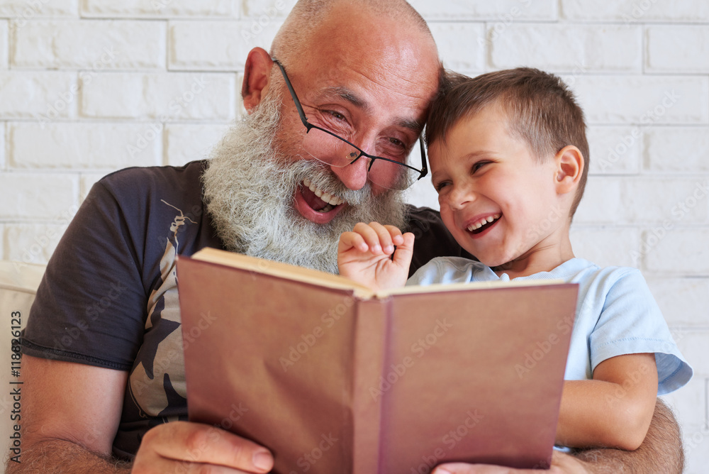 Wall mural bearded aged man and his grandson having fun reading a book toge - Wall murals