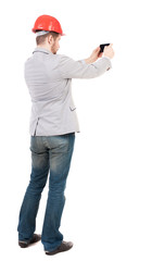 Backview of business man in construction helmet stands and enjoys tablet or using a mobile phone. Standing young guy. Rear view people collection.  backside view of person.  Isolated over white