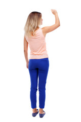 Back view of beautiful woman welcomes. Young teenager girl hand waving from. Rear view  people collection.  backside view of person.  Isolated over white background. Blonde in blue pants writes chalk