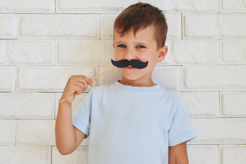 Young gentleman holding paper moustache with rather shrewd look