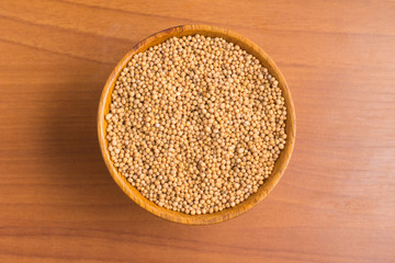Mustard seeds into a bowl over a wooden table