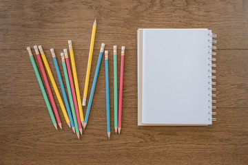 multicolor pencils and blank notebook on wooden background