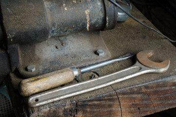old metal wrench and screwdriver lying on a dusty wooden work table