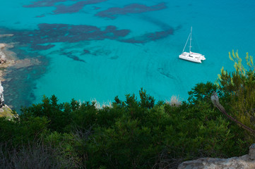 Formentera, Isole Baleari: un catamarano nel Mar Mediterraneo con vista sulla macchia mediterranea...