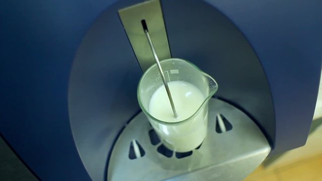 Glass with milk in laboratory equipment for testing dairy products. Analysis of milk sample on modern equipment. Food quality test. Analysis of dairy products. Food quality control equipment
