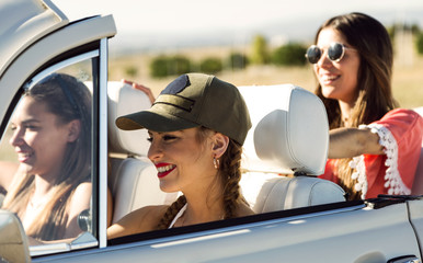 Three pretty young women driving on road trip on beautiful summe