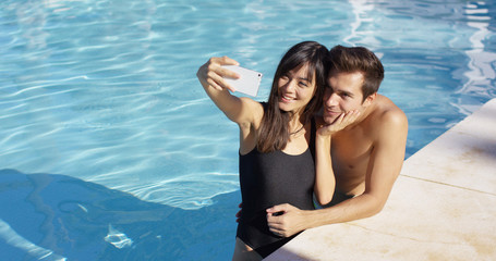 Handsome couple take photo while standing in pool and smile as the sun shines overhead