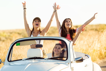 Three pretty young women driving on road trip on beautiful summe