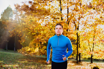Fototapeta na wymiar Young handsome athlete running outside in sunny autumn nature