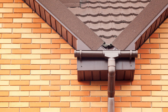 New brown rain gutter with natural metal tile on brick house