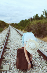 Mujer joven con una maleta esperando en las vías del tren 