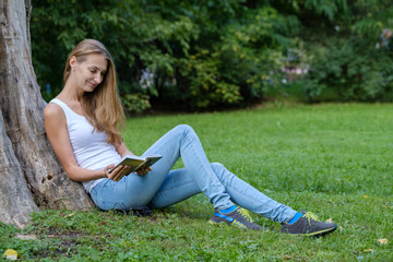 Naklejka na ściany i meble Young woman reading a book in the park and dreaming