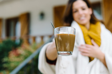 Woman offering cup of coffee outside home on autumn cold day.