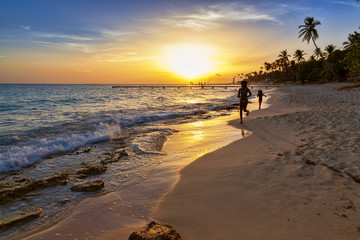 Silhouette of children running along the coastline. Caribbean sea beach sunset. Tropical beach in Caribbean sea, Dominican Republic. Couple are waiting sunset in Caribbean beach. .