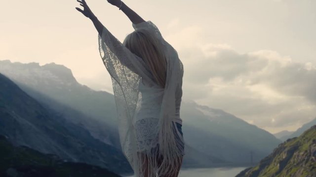 Athletic girl is dancing on the top of the world, beautiful mountains and blue sky on the horizon. She is trying to catch the wind.