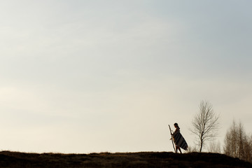 silhouette of woman in poncho walking on hill among
