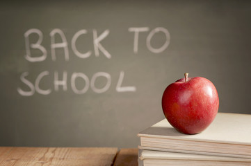 School books and apple against blackboard