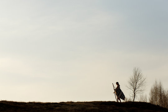 Silhouette Of Woman In Poncho Walking On Hill Among