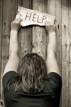 A girl holding a sheet of paper on which is written "help". Girl stands with his back.