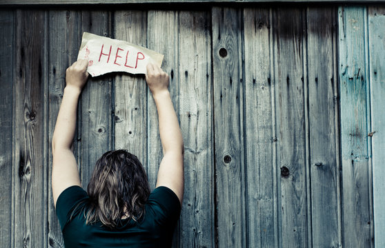 A girl holding a sheet of paper on which is written "help". Girl stands with his back.