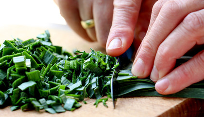 Cutting leek on wood chop board .