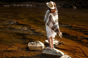 beautiful woman traveler back standing on rocks in river, wearin