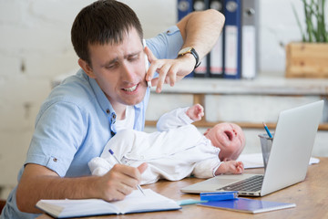 Portrait of young stressed dad trying to work and talk on phone while sitting with his newborn babe...