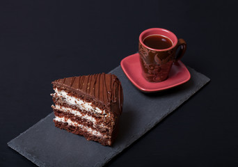 Piece of chocolate cake and cup of coffee on slate plate on blac