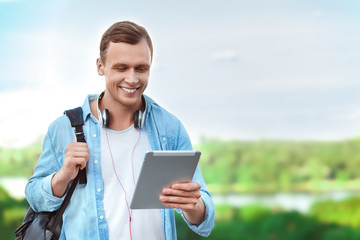 Happy male student holding tablet and smiling while standing on background of city
