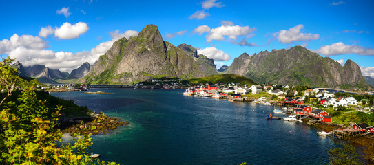 Reine in Lofoten Islands, Norway, with traditional red rorbu huts under blue sky with clouds.  - obrazy, fototapety, plakaty