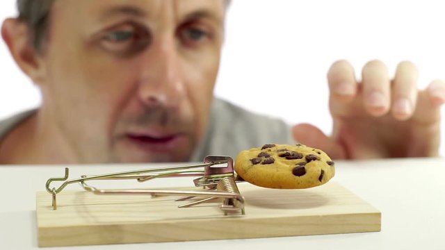 Close up shot of a man looking eagerly at eating a sweet cookie that is in a mouse trap which indicates that he should not eat it or is on a diet.