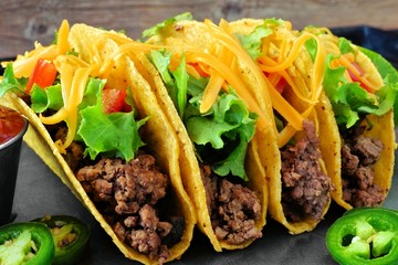 Group of hard shelled tacos with ground beef, lettuce, tomatoes and cheese close up - obrazy, fototapety, plakaty