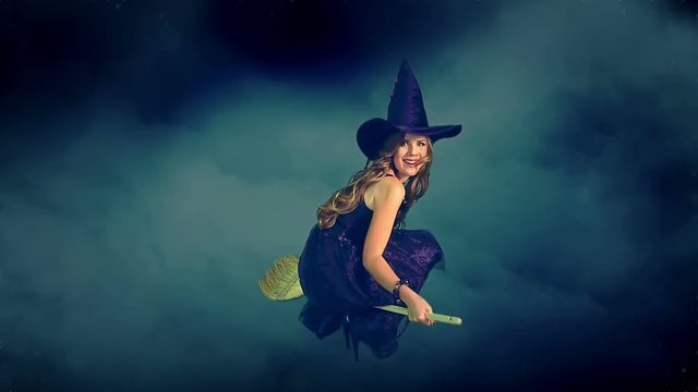 Beautiful young witch flying on broom breaking through cloud mass. Halloween witch wearing witch hat.