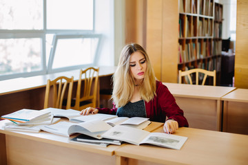 Concentrated attractive female student sitting at desk in old university library preparing for exam and reading books. Education process.