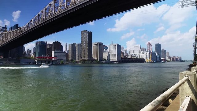 A daytime establishing shot of the Ed Koch Queensboro Bridge between Manhattan and Brooklyn as a speed boat passes underneath.  	