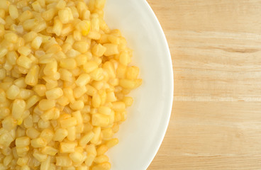 Shoepeg white corn with a butter sauce on a dish atop a wood table.