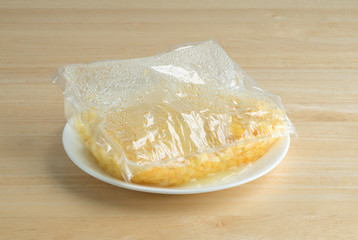Shoepeg white corn with a butter sauce in a bag that has been cooked on a plate atop a wood table.