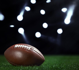 American football ball on a green grass on dark background and spotlight with laser rays